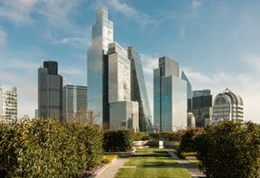 Landscaped rooftop garden overlooking London's financial district, with modern glass skyscrapers rising against a bright blue sky.
