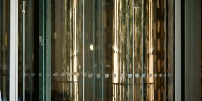 Reflective glass panels create an abstract pattern of light, texture and vertical lines within a contemporary office building.