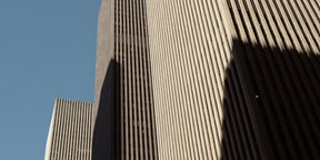 Upward view of Rothschild & Co’s New York office at Avenue of the Americas, showing the modern skyscraper façade rising between neighbouring high-rise buildings against the sky.