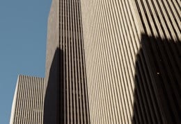 Upward view of Rothschild & Co’s New York office at Avenue of the Americas, showing the modern skyscraper façade rising between neighbouring high-rise buildings against the sky.