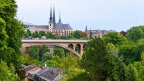 View or church spires in Luxembourg with bridghe over a tree-lined river gorge in the foreground