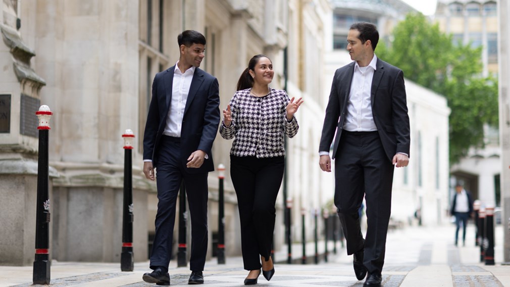 Three young professionals walking in conversation down a narrow street in the City of London