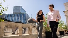 Two colleagues talking on a rooftop terrace overlooking the City of London skyline.