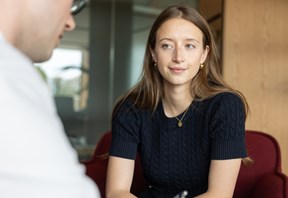Person seated in an office meeting area, listening and taking notes