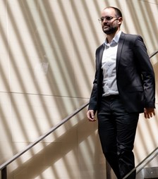 A person in a suit walks down a modern, sunlit staircase, exuding confidence. Tall windows create diagonal light patterns on the walls.