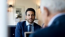 2 middle aged men in a suits looking at each other