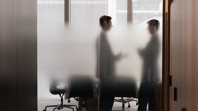 Silhouette of two colleagues stood in a modern meeting room.