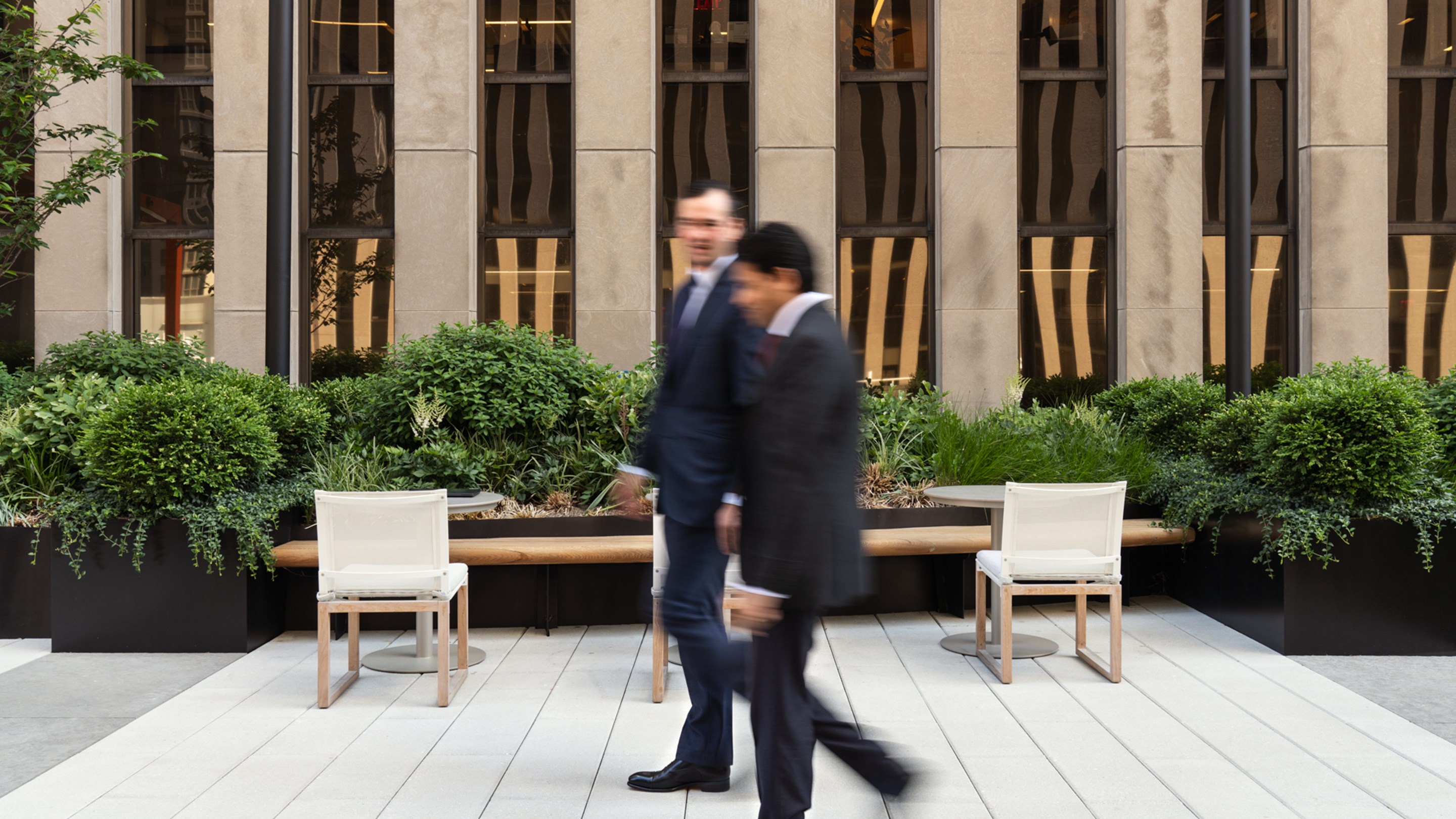 Two people walking in conversation on a sunny roof terrace with a modern skyscraper behind