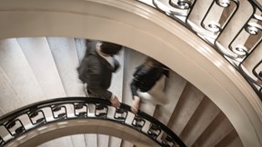 A newlywed couple stands on a grand spiral staircase. The elegant, curved design of the stairs adds a sense of romance and sophistication to the scene.