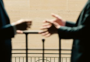 Two people are standing against a railing, partially visible, engaging in conversation. Their hands are gesturing expressively, conveying discussion.