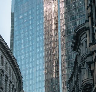Reflections in a modern office tower, with older stone architecture in the foreground
