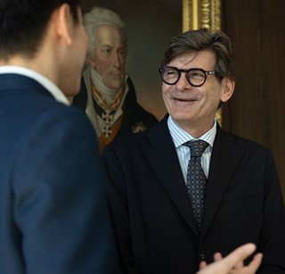 Two colleagues in business attire conversing in an office environment, with one colleague gesturing while speaking.