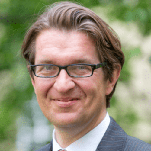 man in glasses with trees behind him