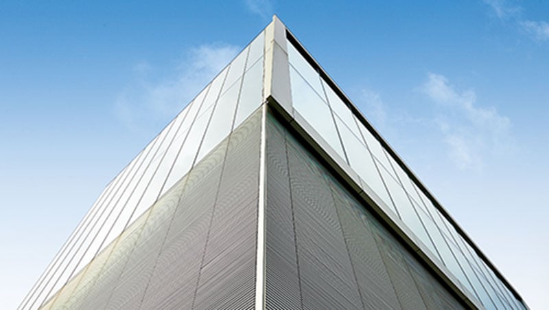 Corner of a modern glass office building viewed from below against a blue sky.