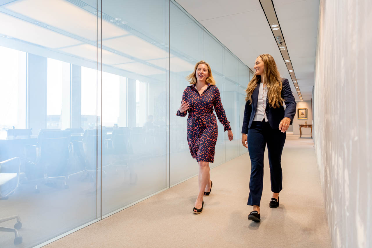 Two colleagues walking down a hallway next to meeting rooms