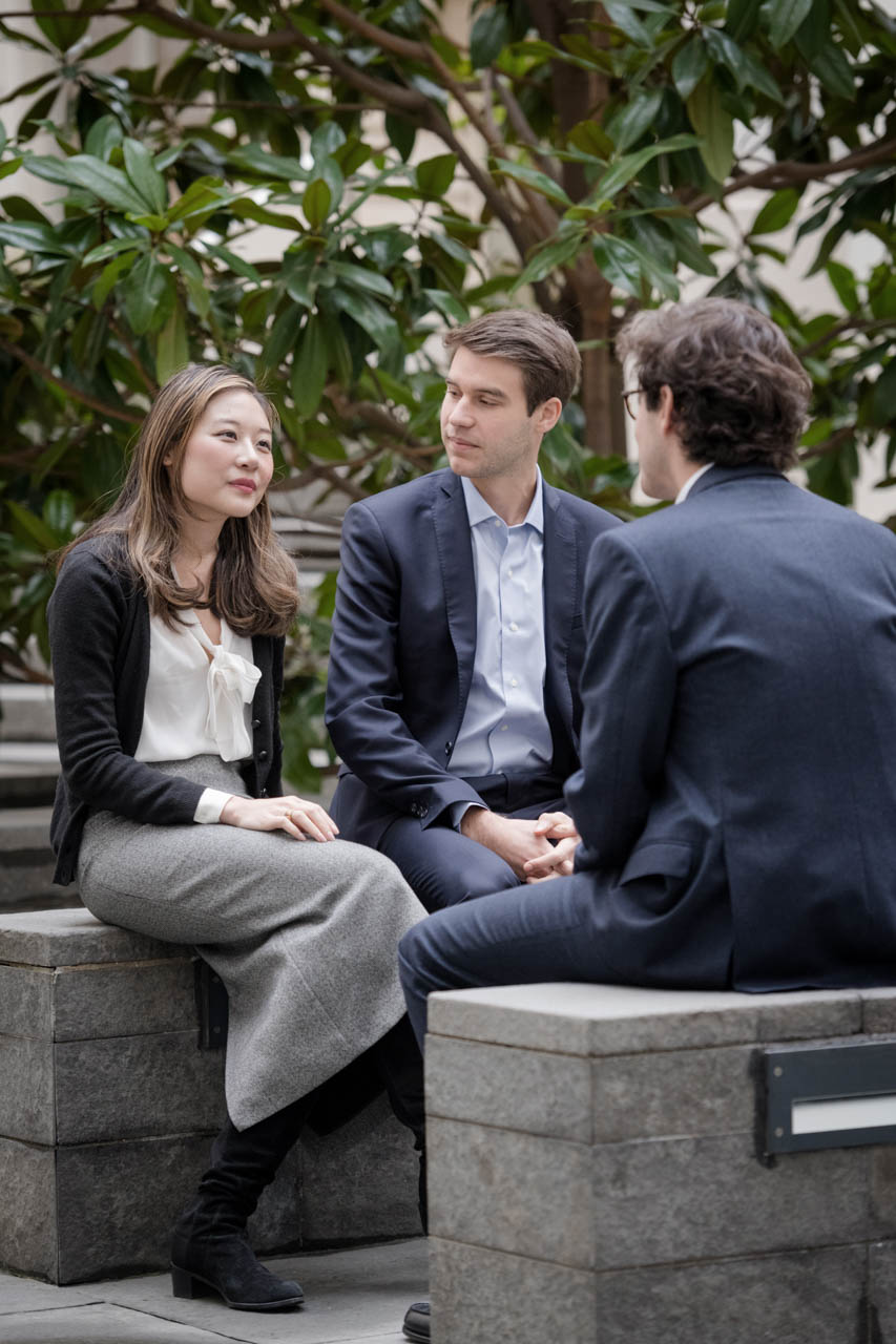 Two men and a woman siting on stone benches outside, engaged in conversation 