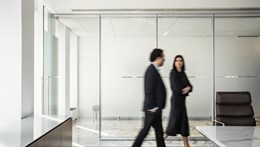 Image of two people walking through the office of Rothschild & Co with a white curtain in the background