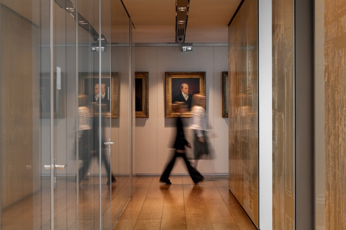 Image of two people walking through a corridor at Rothschild & Co with family portraits behind them