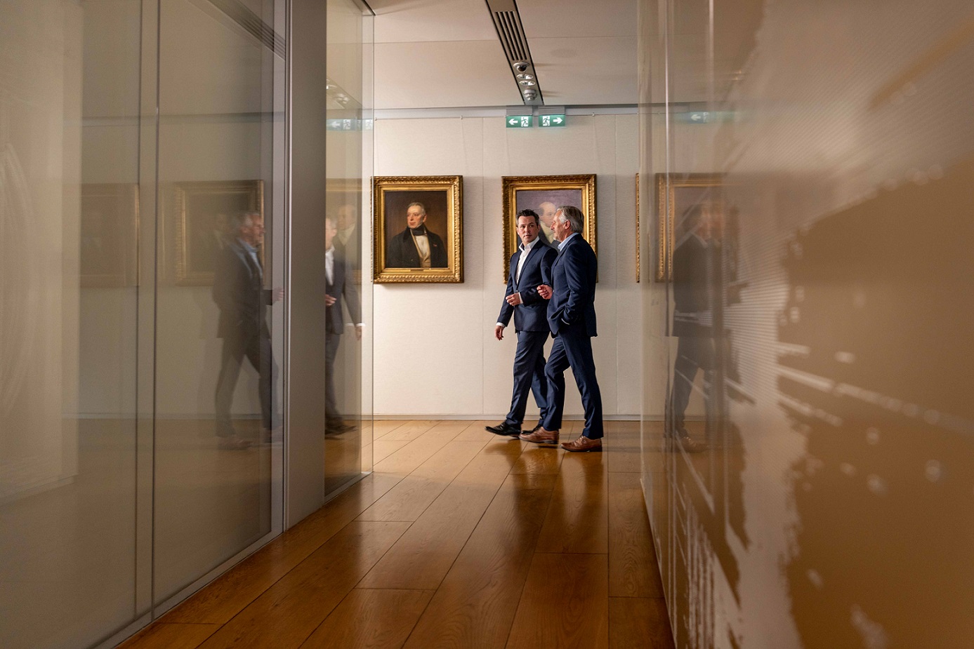 Two people walking next to multiple family paintings 