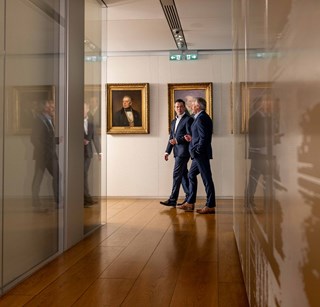 Two people walking next to multiple family paintings 