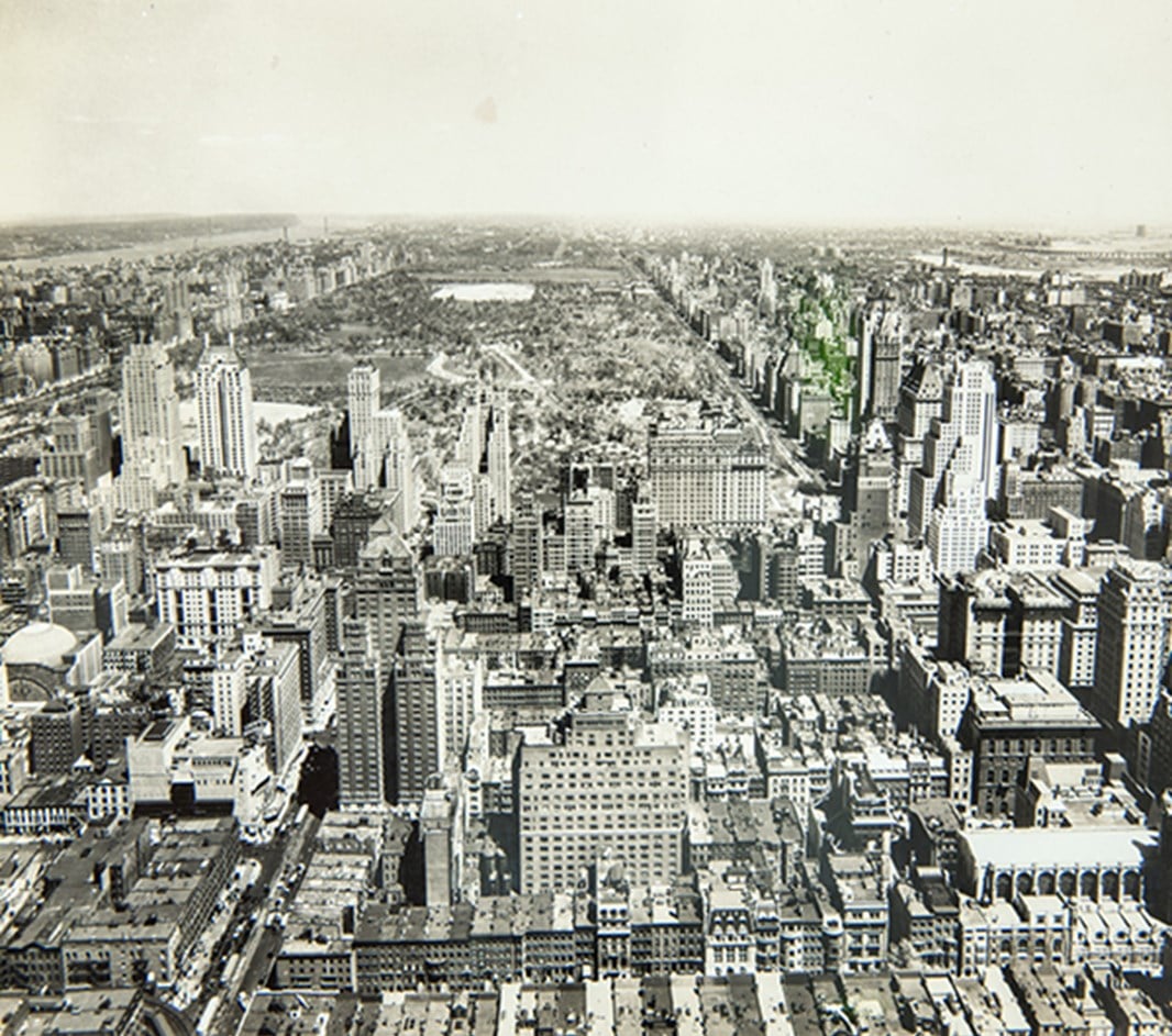 Black-and-white photograph of the New York City skyline, showing a dense cluster of skyscrapers and high-rise buildings viewed from across the water