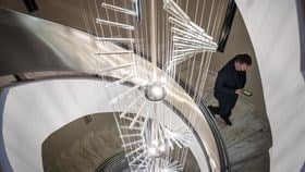 A photograph of the sculpture in Rothschild & Co’s Zurich office that goes through the centre of a spiral staircase. A man walks down the stairs in a suit looking down at his phone which is in his right hand.