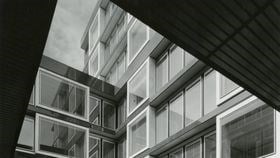 A black and white photo showing New Court from below, with a geometric right angle cut out from part of the building blocking the top part of the image. The building is mainly formed of windows of horizontal, rectangular glass.